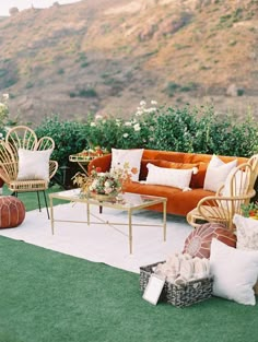 an outdoor seating area with wicker furniture and flowers on the grass in front of a mountain