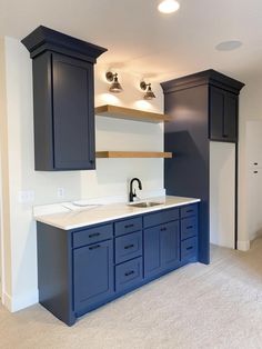 an empty kitchen with dark blue cabinets and white counter tops, along with beige carpeting