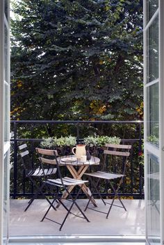 an open door leading to a balcony with table and chairs on it, overlooking the trees