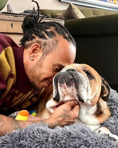 a man with dreadlocks kisses his dog on the nose while laying on a gray rug