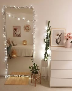 a room with a mirror, plant and pictures on the wall next to it is lit up by string lights