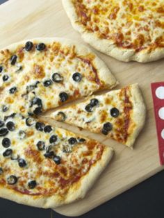 two pizzas with black olives and cheese on a cutting board next to a red dice