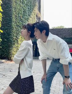 a man and woman standing next to each other on a brick floor in front of a building