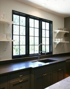 an empty kitchen with black cabinets and white counter tops is pictured in this image, there are two windows above the sink