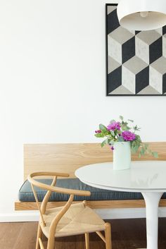 a white table with flowers in a vase on it next to a wooden bench and chair