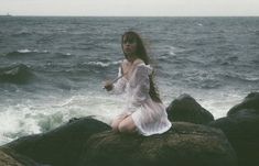 a woman sitting on top of a rock near the ocean