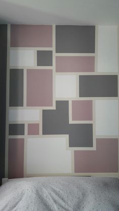 a bed with a white comforter in front of a wall painted with squares and rectangles