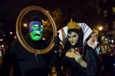 two people dressed in costumes and masks holding up a mirror with a face painted on it