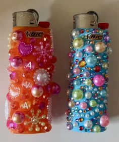 two lighters are decorated with colorful beads and pearls on the sides, one has a keychain that is attached to it