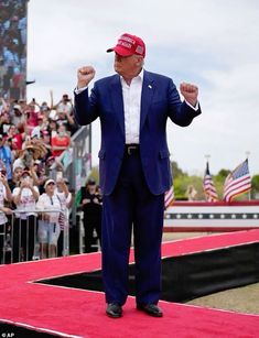 a man in a blue suit and red hat standing on a stage with his arms up