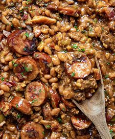 beans and sausage are mixed together in a dish with a wooden spoon on the side