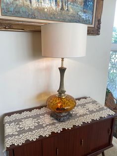 a table with a lamp on top of it next to a painting and framed pictures