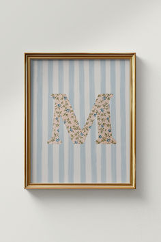 the letter m is made up of flowers and leaves in a gold frame on a striped wall