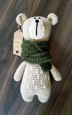 a crocheted teddy bear with a green scarf around it's neck on a wooden floor