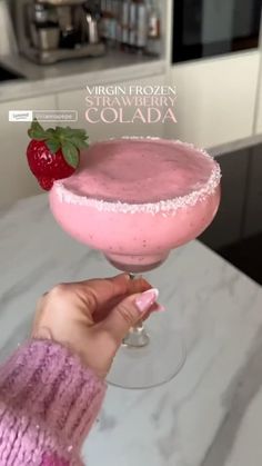 a person holding up a pink drink in a glass with strawberries on the rim