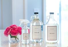 three bottles are sitting on a table with pink flowers in the vases next to them