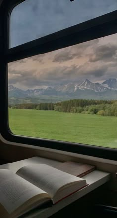 an open book sitting on top of a window sill next to a green field