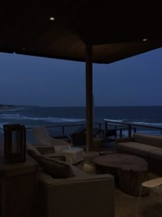 an outdoor living area with couches and chairs overlooking the ocean at night, lit up by lights