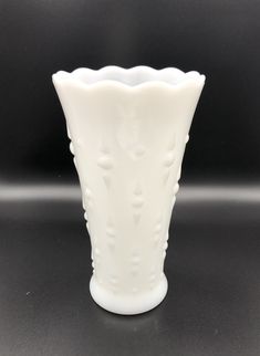 a white glass vase sitting on top of a table next to a black wall and floor