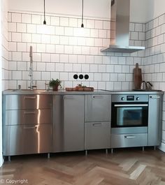 a kitchen with stainless steel appliances and wood flooring on the walls, along with white subway tiles