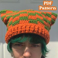 a woman with green hair wearing an orange and green knitted cat hat