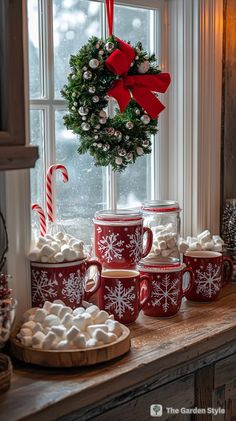 red and white mugs are sitting on a window sill with candy canes