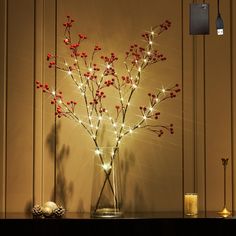 a vase filled with red berries sitting on top of a table next to a candle