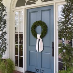 a blue front door with a wreath and white bow hanging on it's side