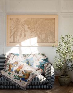 a living room with a couch, potted plant and framed artwork on the wall