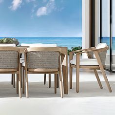 an outdoor dining table with four chairs next to the ocean and blue sky in the background