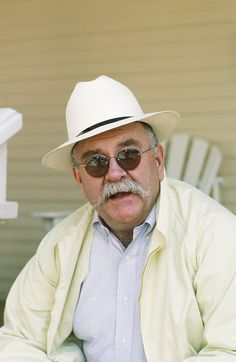 an older man wearing sunglasses and a white hat sitting on a porch chair stock photo