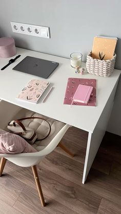 a white desk topped with a laptop computer sitting on top of a wooden floor next to a pink pillow