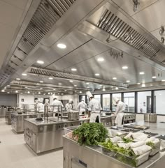 two chefs are preparing food in a large commercial kitchen with stainless steel counters and overhead lighting