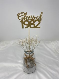 a glass vase filled with baby's breath flowers and a gold class of 1932 cake topper