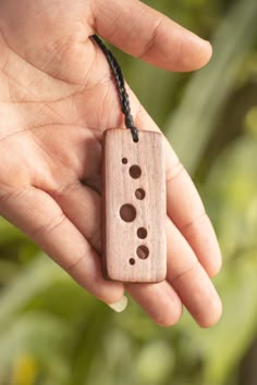 a hand holding a small wooden object with holes in it's middle and two fingers