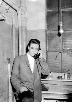 a black and white photo of a man in a suit talking on a cell phone