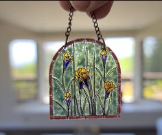 a hand holding a stained glass window with yellow flowers on the outside and blue sky in the background