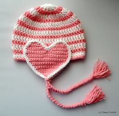 a pink and white knitted hat with a heart on the front, along with a tassel