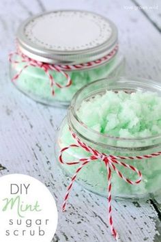 two jars filled with green sugar on top of a white wooden table next to a red ribbon