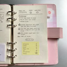 an open notebook with sticky notes attached to the pages, and a pink clipboard next to it