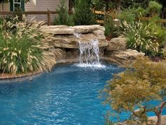 a small pool with waterfall and rock walls in the back yard, surrounded by plants