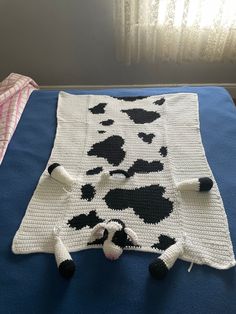 a crocheted blanket with black and white cows on it sitting on a bed