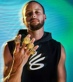 a man holding two gold rings in his hand and wearing a black shirt with white letters on it