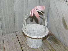 a small white basket with a pink bow on the handle sitting on a wooden floor