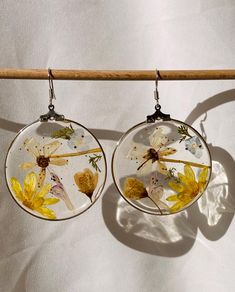 two glass earrings with yellow flowers on them hanging from a wooden stick in front of a white background