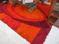 an orange and red rug on the floor in front of a glass table with books