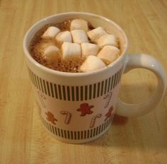 a cup filled with hot chocolate and marshmallows on top of a wooden table