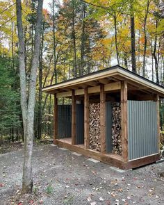 a small shed in the middle of a forest with lots of wood stacked on top of it