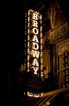 the broadway sign lit up at night in front of an old building with lights on it