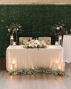 a table with candles and flowers on it in front of a wall covered in greenery